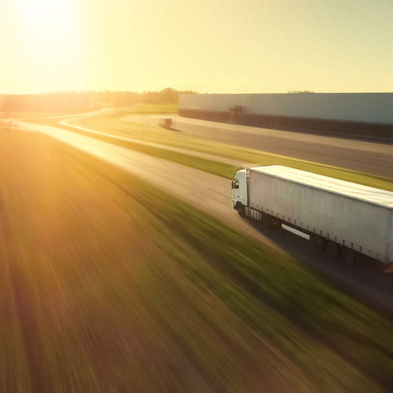 A white semi truck driving down an empty highway during sunset.