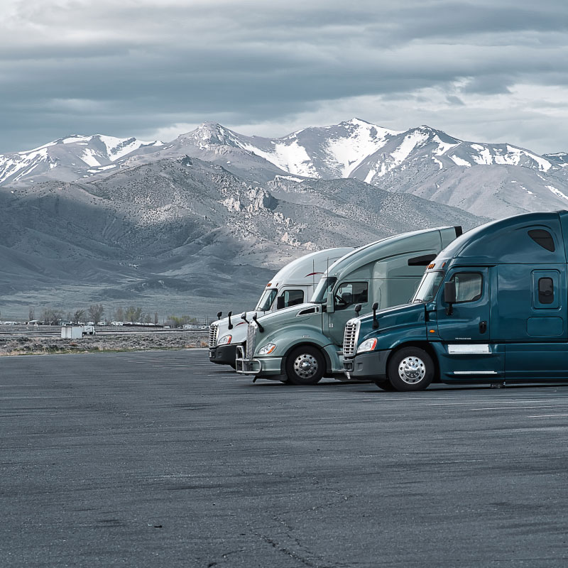 Three semi trucks parked in front of mountains.