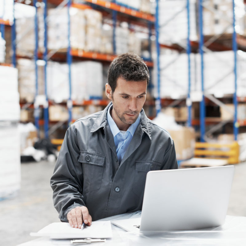 Male employee working on computer in warehouse.