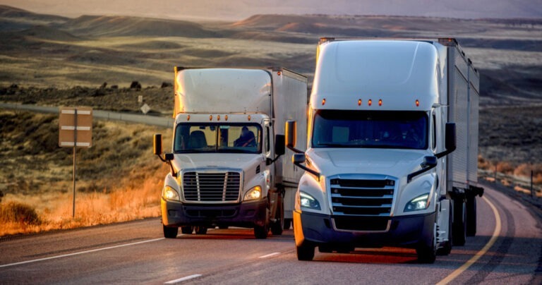 Two white semi trucks driving down highway.