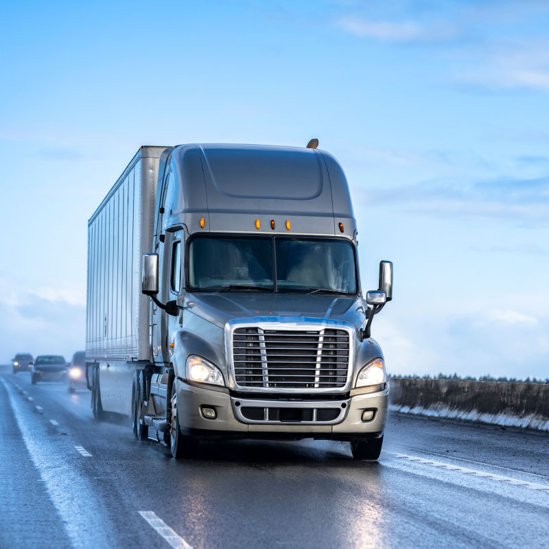 Gray semi truck driving down a winter highway.