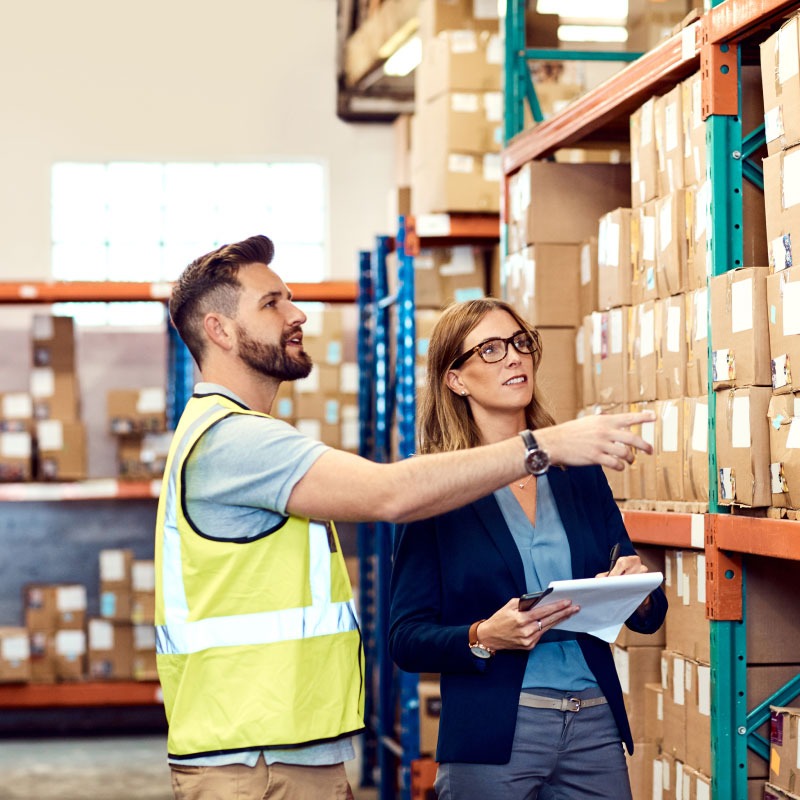 Dos empleados de almacén conversan sobre el inventario.