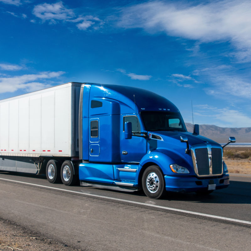 Blue semi truck driving down sunny highway.