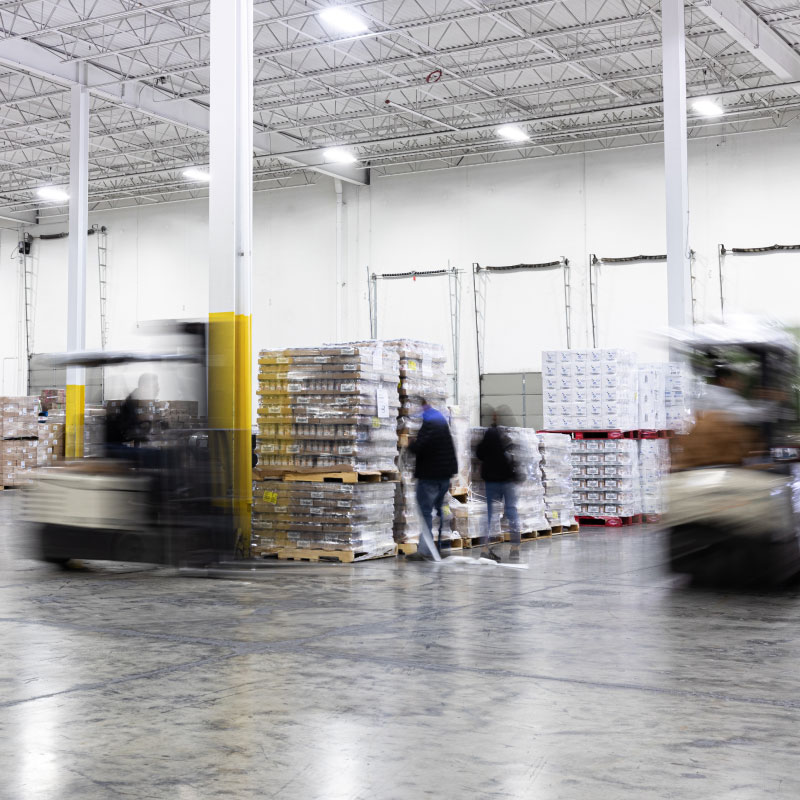 Blurred-motion of warehouse employees moving freight around warehouse.