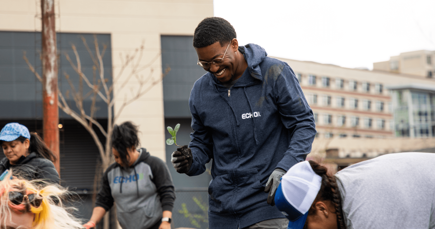 An Echo employee holding a small outdoors plant while participating at Echo's urban gardening event.