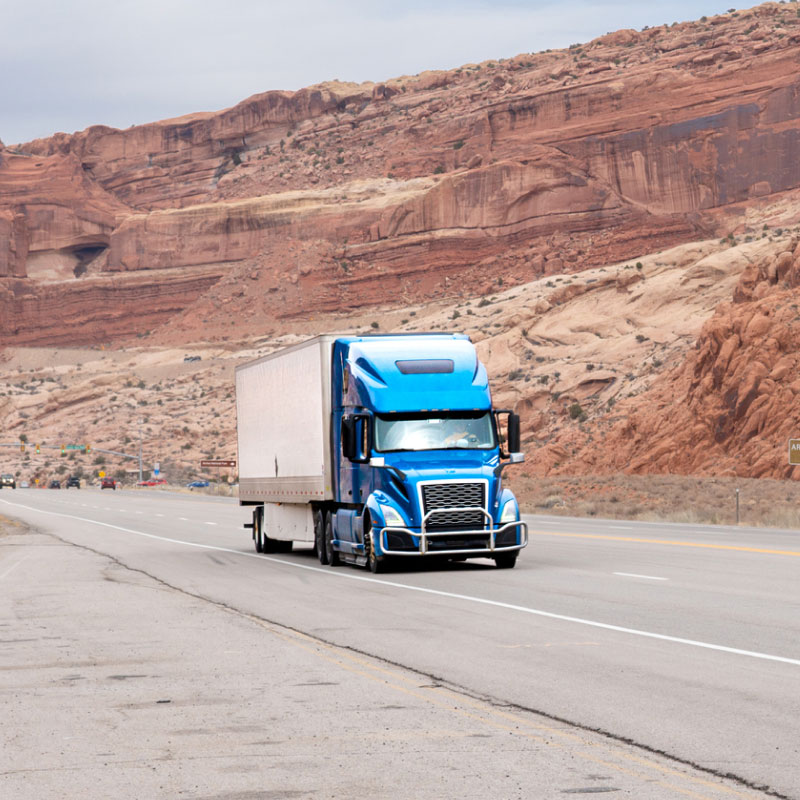 Blue semi truck driving down highway in desert