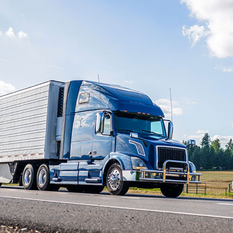 A blue and white semi truck driving down an empty road.