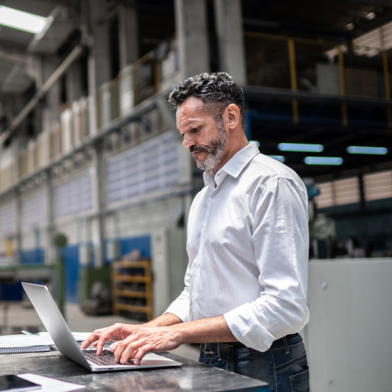 A man in a warehouse setting on his laptop.