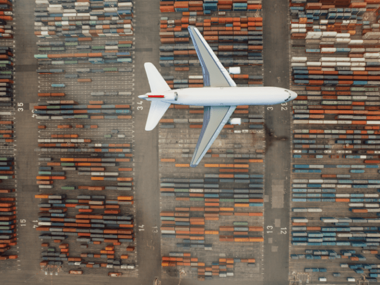 Airplane flying over shipping container port.