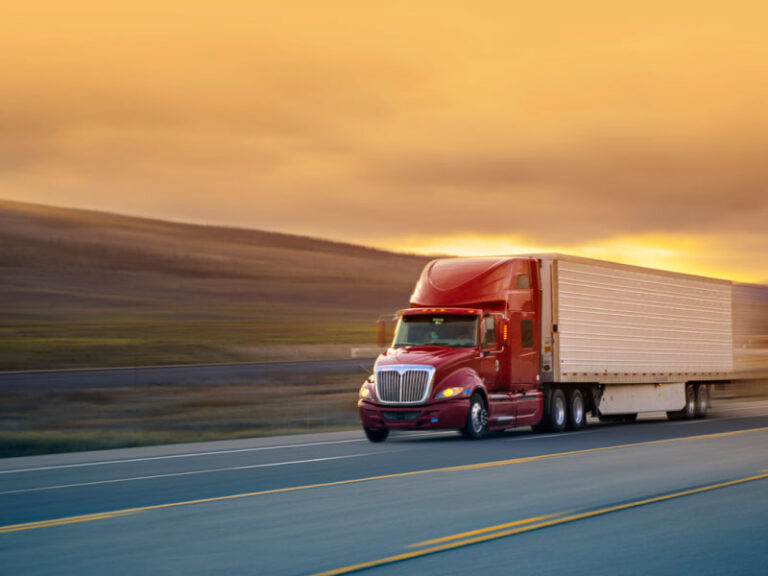 A red semi-truck driving down a road to deliver freight quickly.