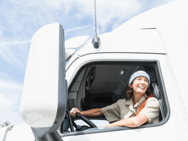 A female truck driver smiling out of the driver seat window
