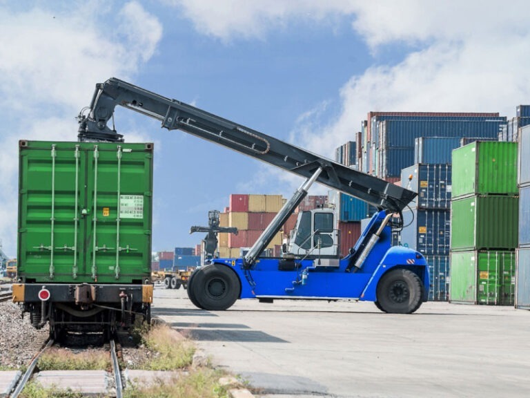 An intermodal container being forklifted off a cargo train to be transported to a semi truck.