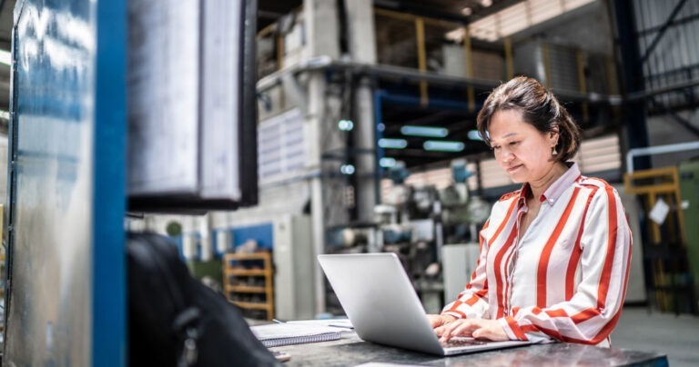 A shipper working on their laptop inside a factory.