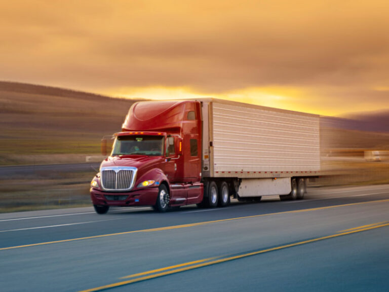 Red and white semi truck going down the highway at sunset.