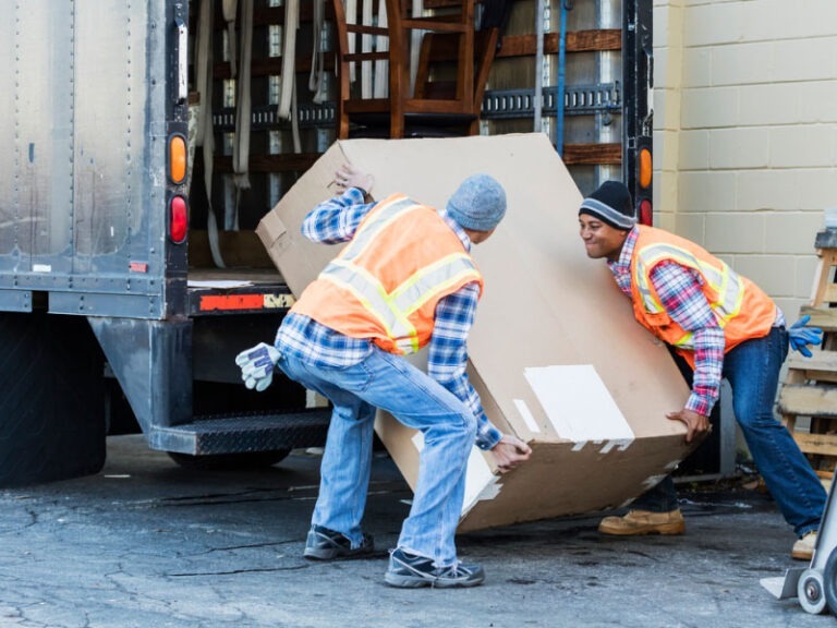 Two workers moving a box out of their truck to deliver it to their final destination.