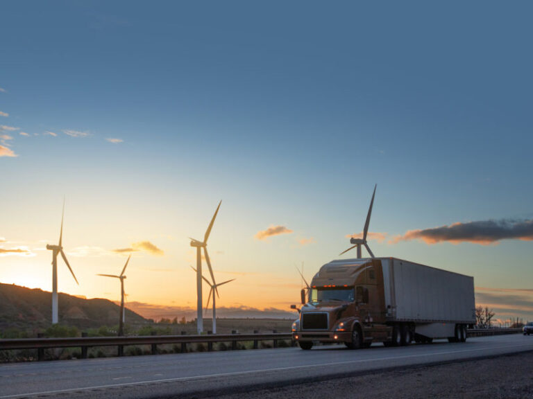 An orange semi truck speeding in front of wind turbines in Utah, USA.