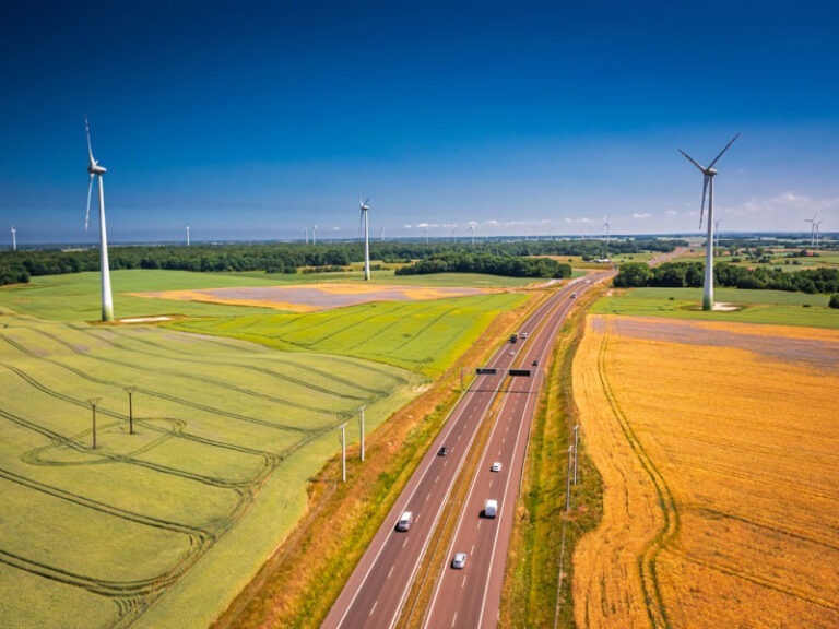 Aerial view of golden field and wind turbines near highway.