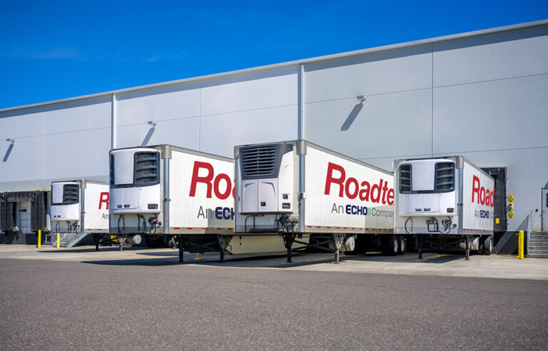 Multiple refrigerated truck beds with Roadtex, an Echo Company logo stationed at warehouse loading dock.