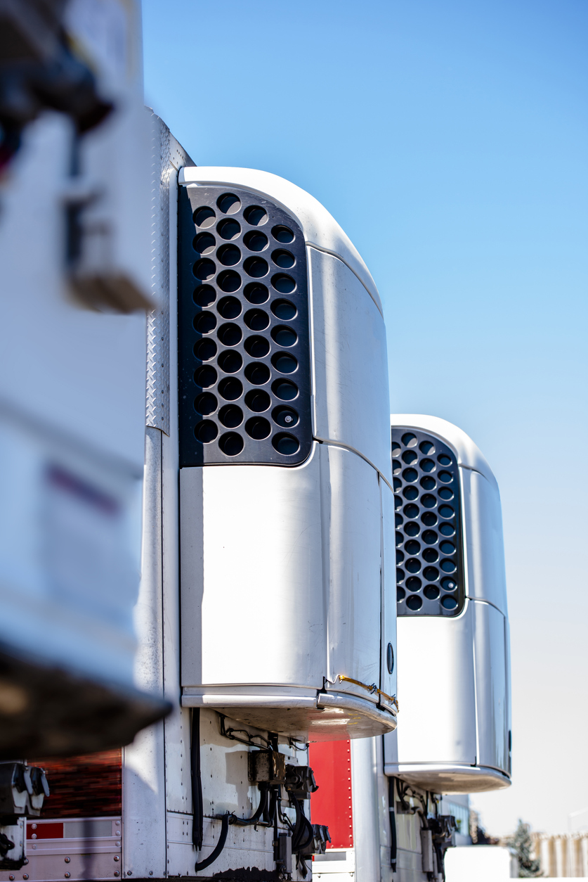 A line of refrigeration semi truck trailers in a row at a warehouse parking lot.