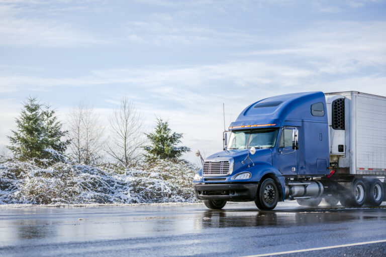 A blue temperature controlled semi truck driving down a frozen highway. 