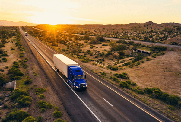 A blue semi truck driving down a highway located in the desert. 