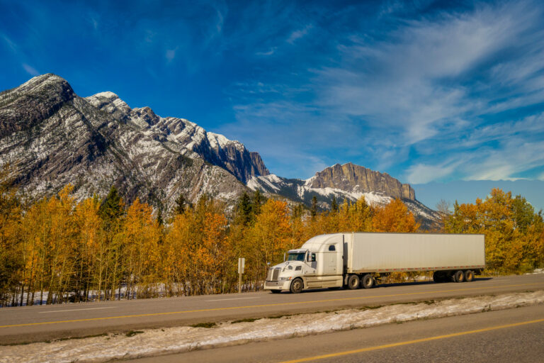 A white semi truck driving down a highway next to mountains. 