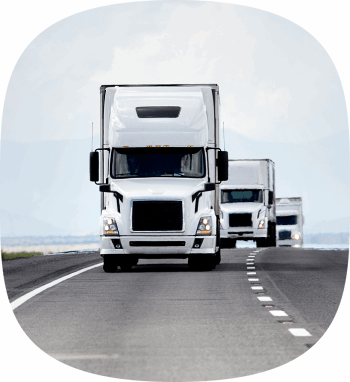 Three white semi trucks driving down the highway.