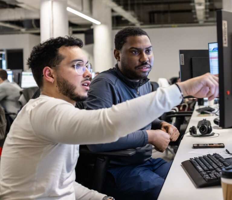 A sales manager training a new sales rep at their desk.